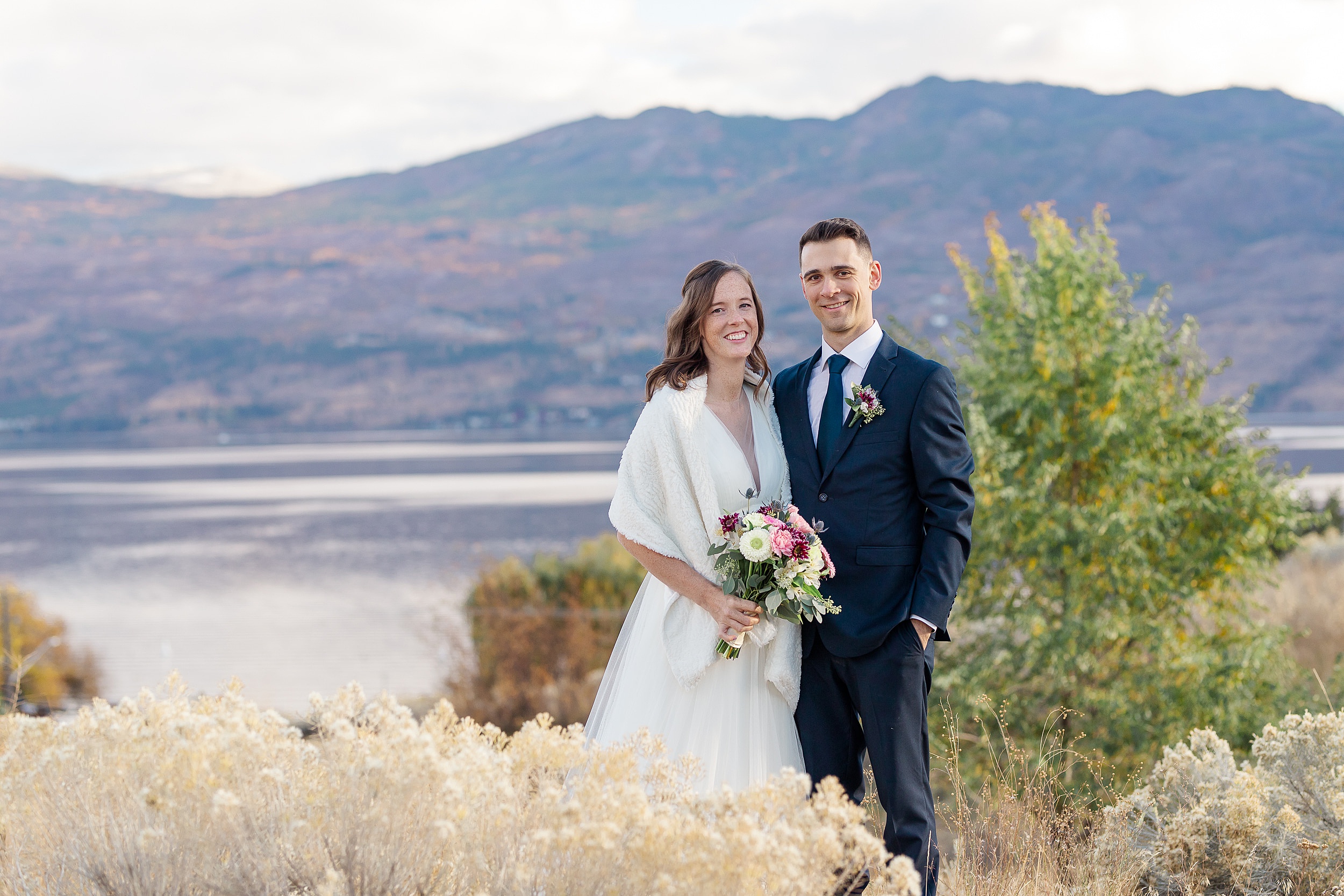 bride and groom smiling with the lake and mountains behind them Sanctuary Gardens Kelowna