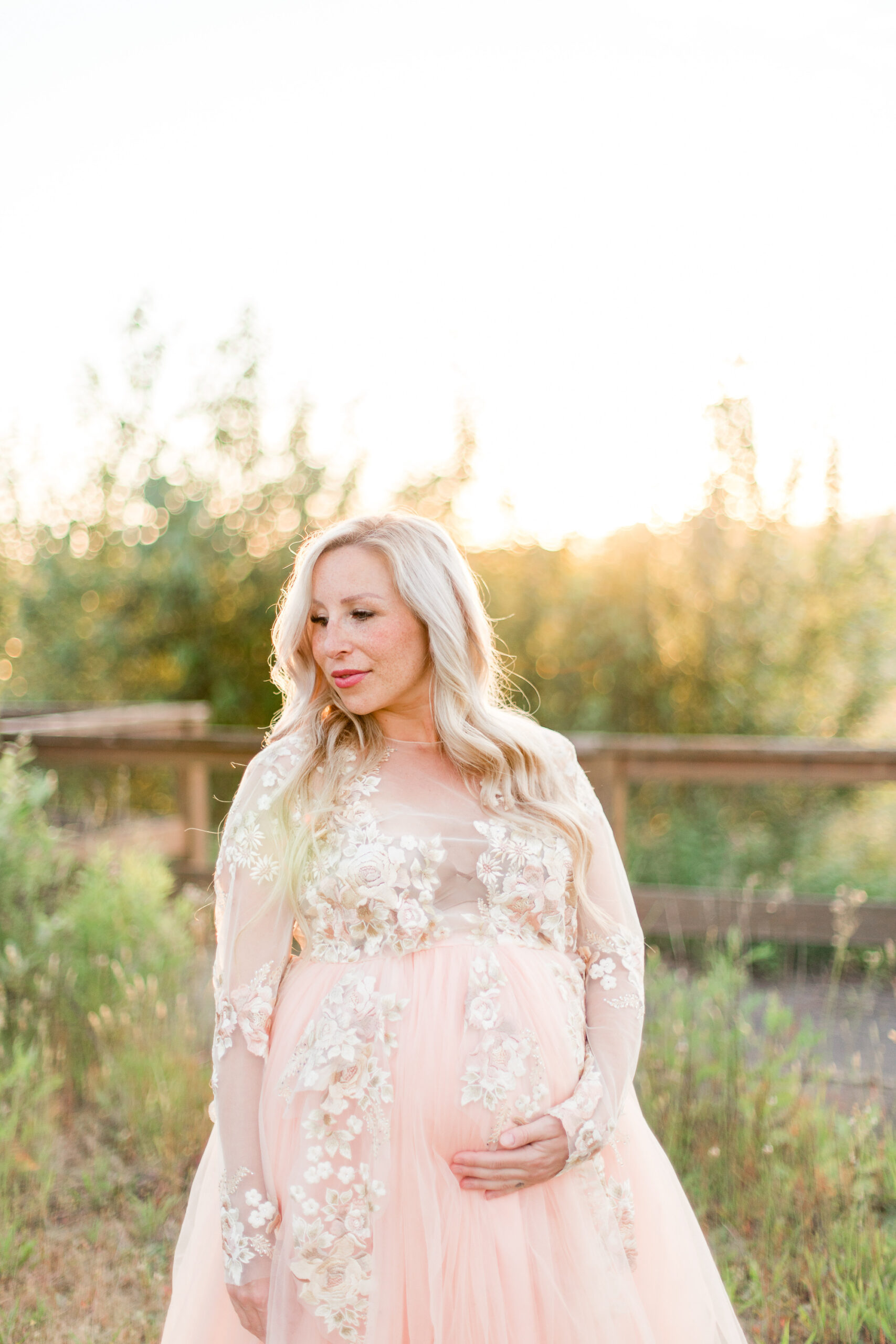 mom to be in pink maternity gown holding her bump at sunset Kelowna doulas