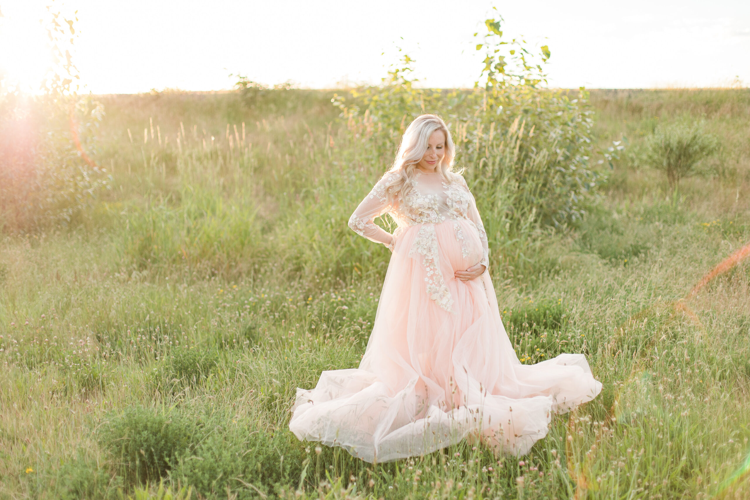 mom to be in pink sparkly maternity gown cradling her bump in a field Kelowna doulas