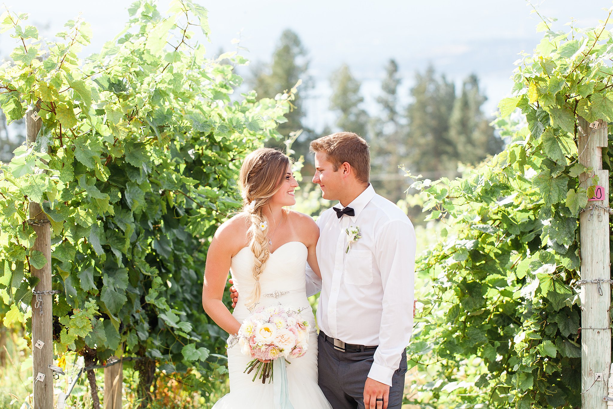 Newlyweds stand in a vineyard staring at each other while holding a white bouquet Covert farms family estate