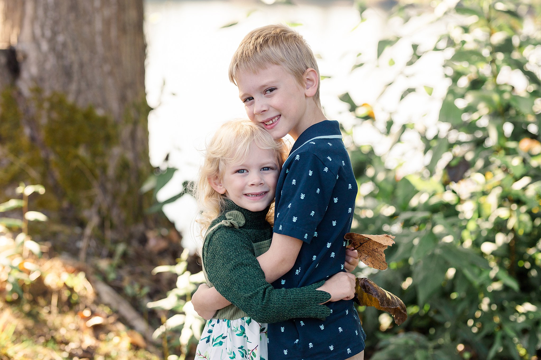 A brother and sister hug in a park while holding some fallen leaves kelowna pediatricians