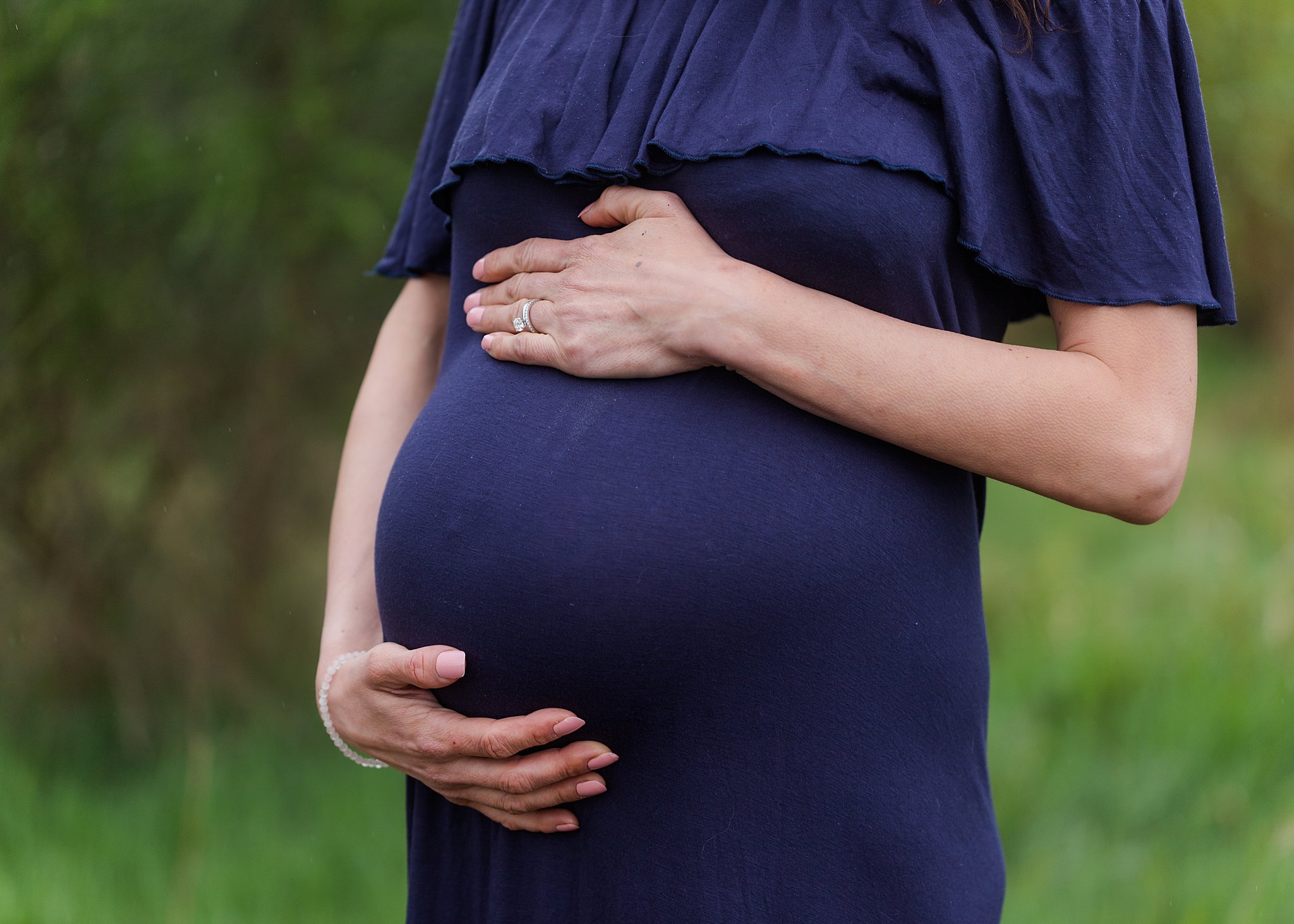 A pregnant woman holds her bump with both hands in a green park maternity clinic penticton