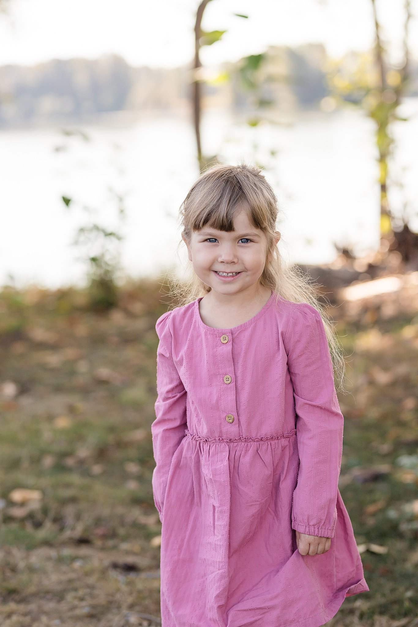 A young girl in a pink dress walks through a park next to a lake things to do in peachland